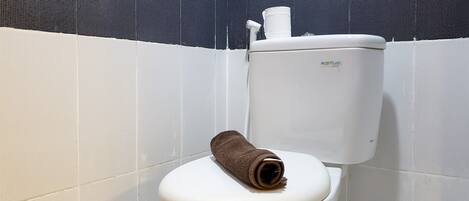 A toilet with a brown towel on the lid, a toilet paper holder, and a white wall with a black and white pattern.