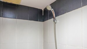 Une douche avec un pommeau flexible dans un coin d’une pièce aux murs recouverts de carreaux blancs et au plafond noir texturé.
