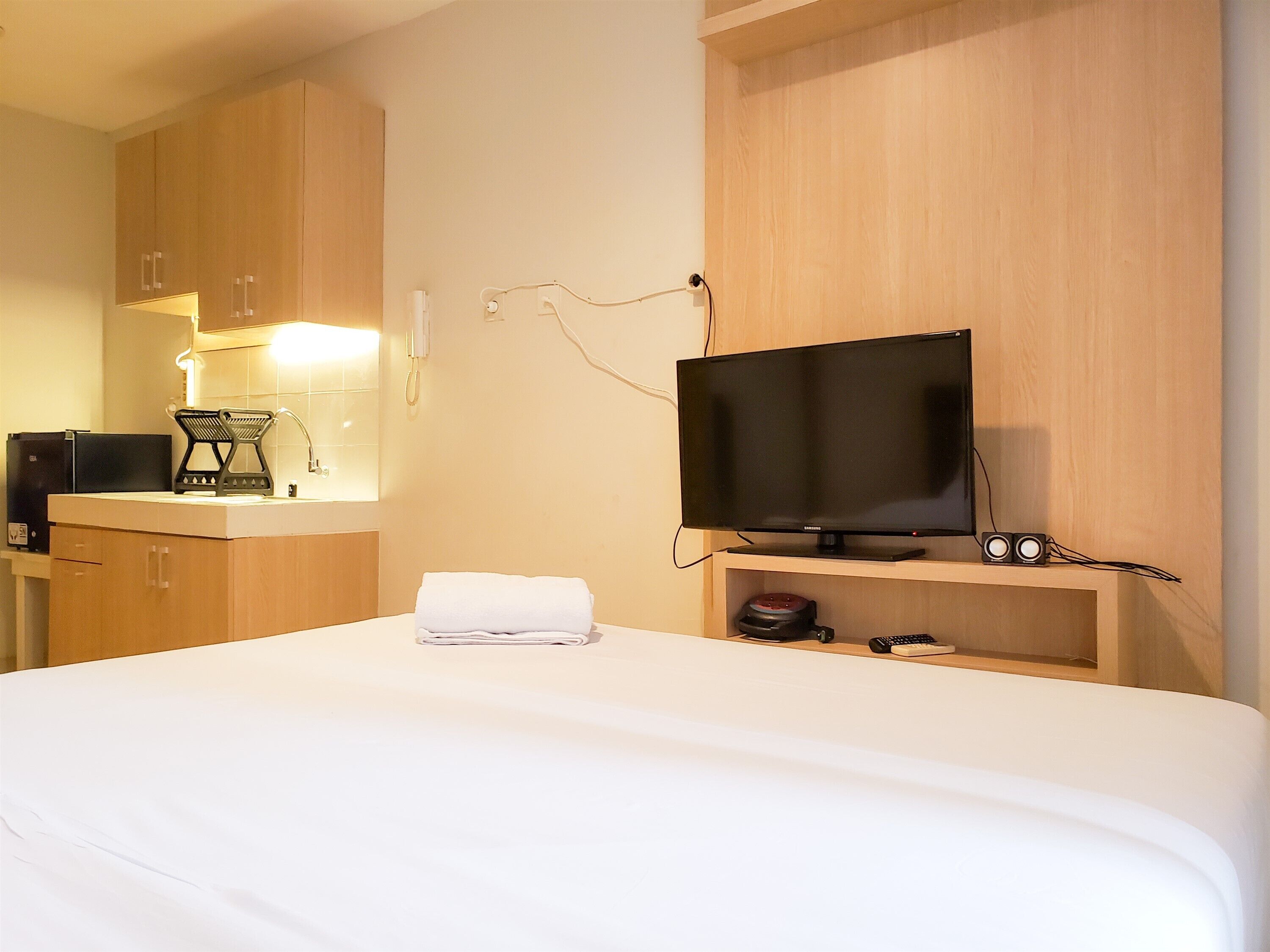 A hotel room with a bed, a television on a stand, a desk with a computer and a telephone, and wooden cabinets.