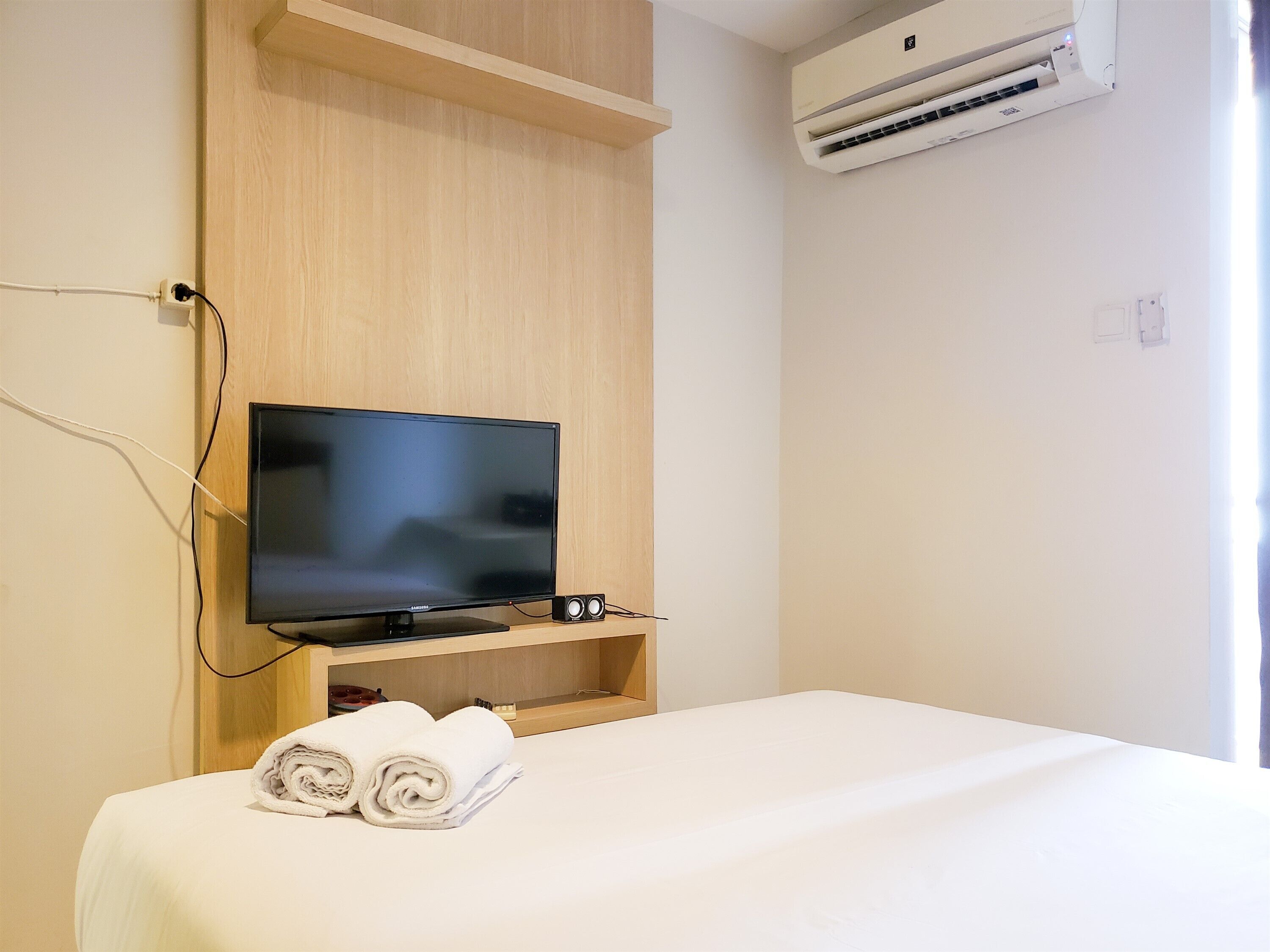 Quarto de hotel com cama, televisão sobre suporte de madeira e ar condicionado na parede.