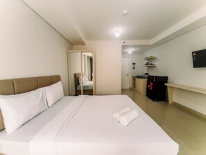 A hotel room with a large bed, a desk, a mirror, and a TV on the wall. - Cozy Studio Room At Barsa City Apartment (Depok)