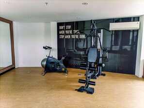 A gym with a stationary bike, a weight machine, and a motivational poster on the wall. - Cozy Studio Room At Barsa City Apartment (Depok)