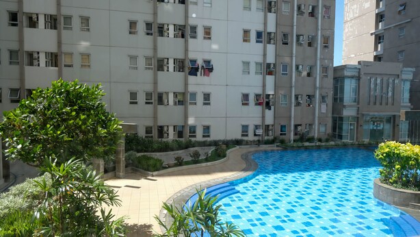 A residential building with multiple balconies, a swimming pool, and surrounding greenery. - Clean And Comfy 2Br Apartment At Puncak Kertajaya (Surabaya)