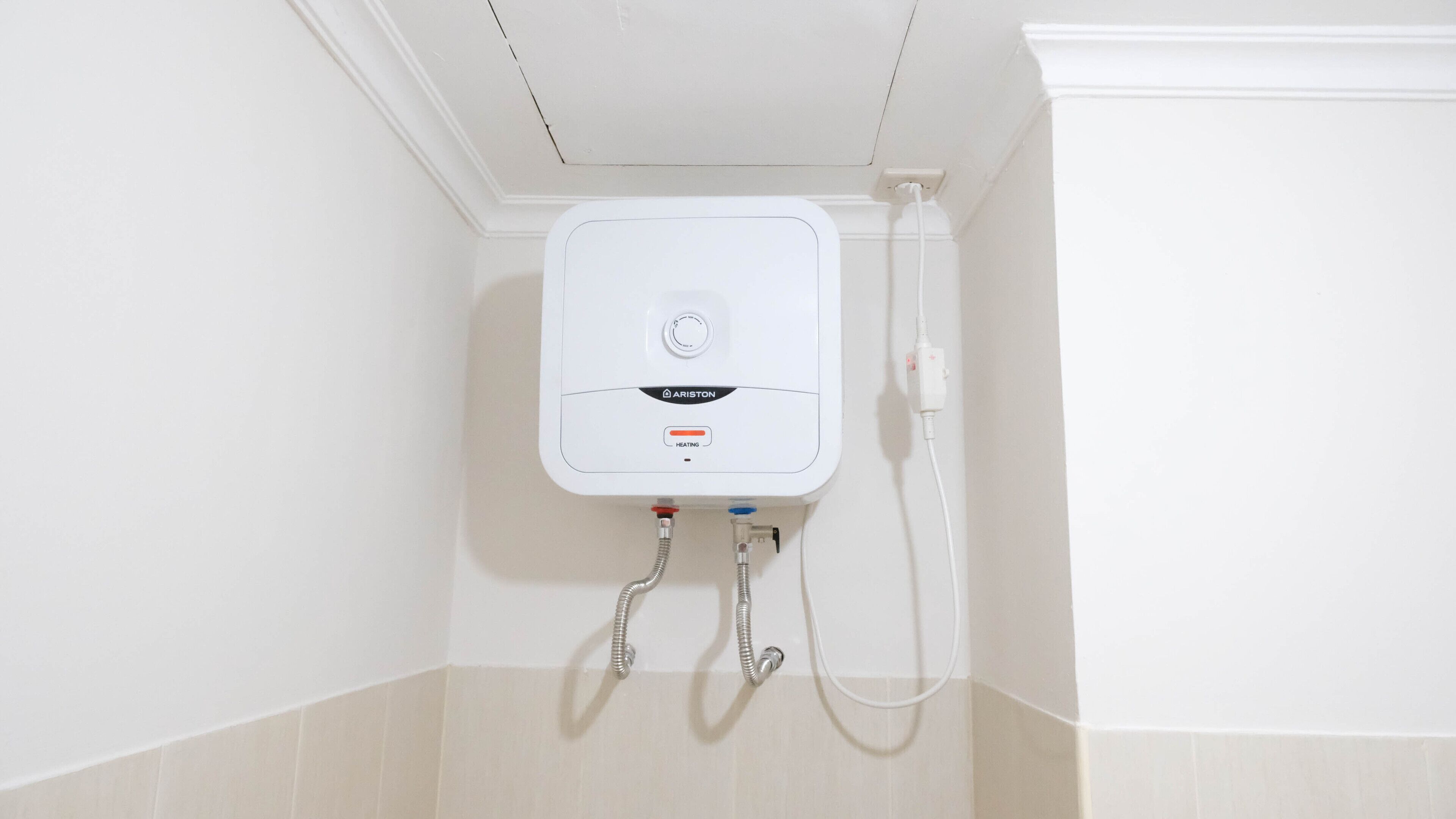 Calentador de agua blanco instalado en una pared, con panel de control y dos mangueras flexibles.