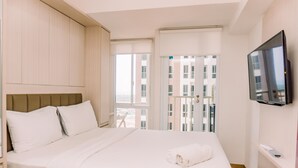 A hotel room with a bed, a TV, and a balcony with a view of buildings. - Simply Look And Comfy Studio At Tokyo Riverside Pik 2 Apartment (Teluknaga)