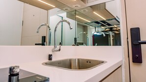 A modern bathroom with a stainless steel sink, a mirror, and a door with a handle. - Simply Look And Comfy Studio At Tokyo Riverside Pik 2 Apartment (Teluknaga)