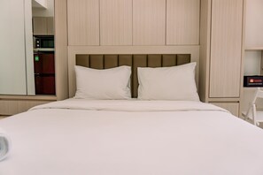 A hotel room with a bed, a wooden headboard, a wardrobe, and a minibar. - Simply Look And Comfy Studio At Tokyo Riverside Pik 2 Apartment (Teluknaga)