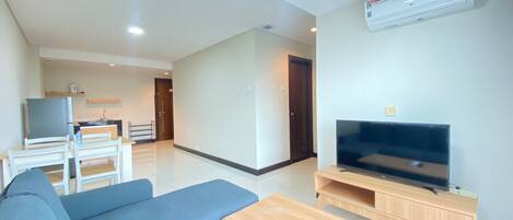 A modern living room with a sofa, TV, and a small table. There is a kitchen area in the background.