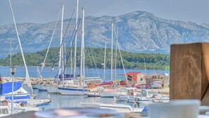 En lysthavn med fortøjede både, et træbord med mad på, og et bjerg i baggrunden.