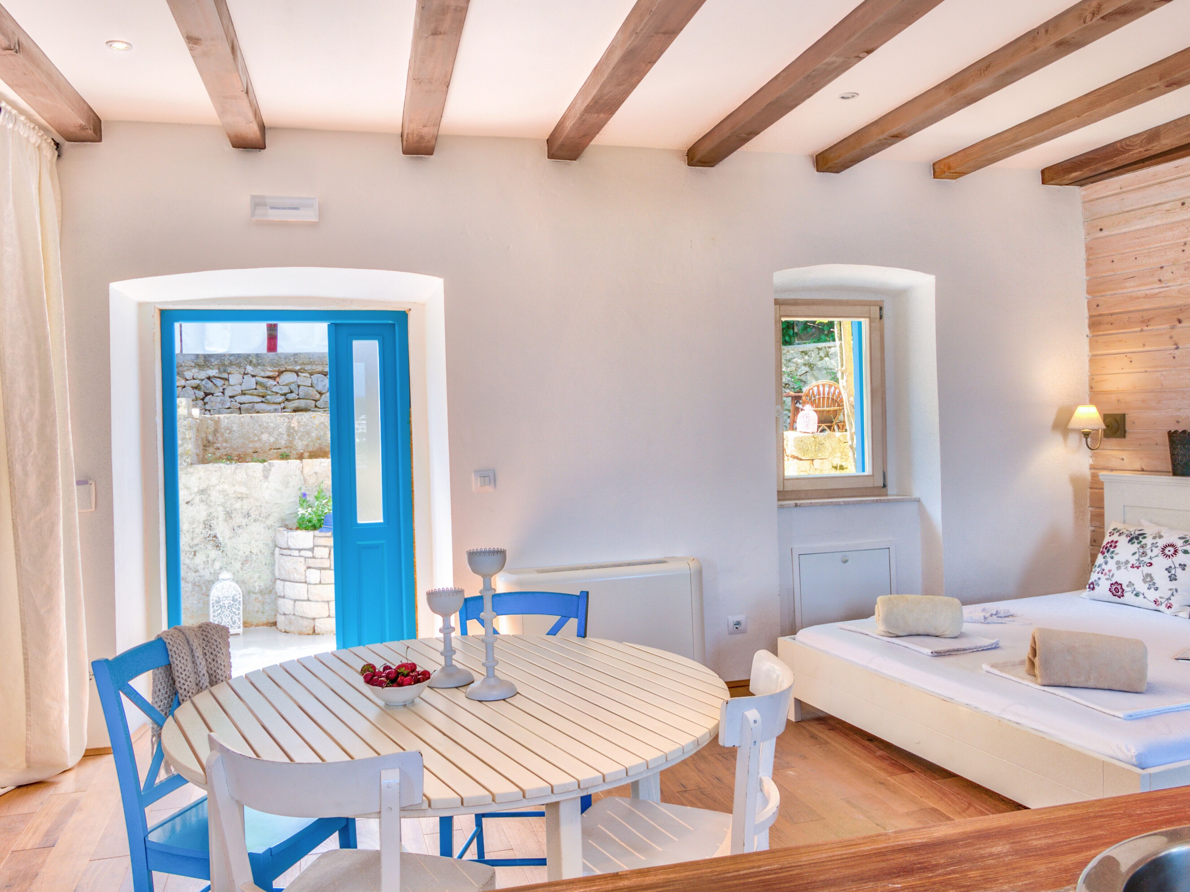 A room with a round wooden table, blue chairs, a white sofa, and a stone wall.