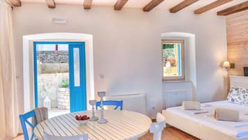 A room with a round wooden table, blue chairs, a white sofa, and a stone wall.