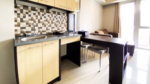 A modern kitchen with wooden cabinets, a checkered backsplash, and a bar area with stools. - Fancy And Nice 2Br Apartment At Skyland City Jatinangor (Hegarmanah)