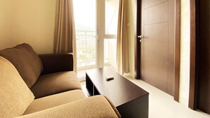 A room with a brown sofa, a small table, and a door. - Fancy And Nice 2Br Apartment At Skyland City Jatinangor (Hegarmanah)