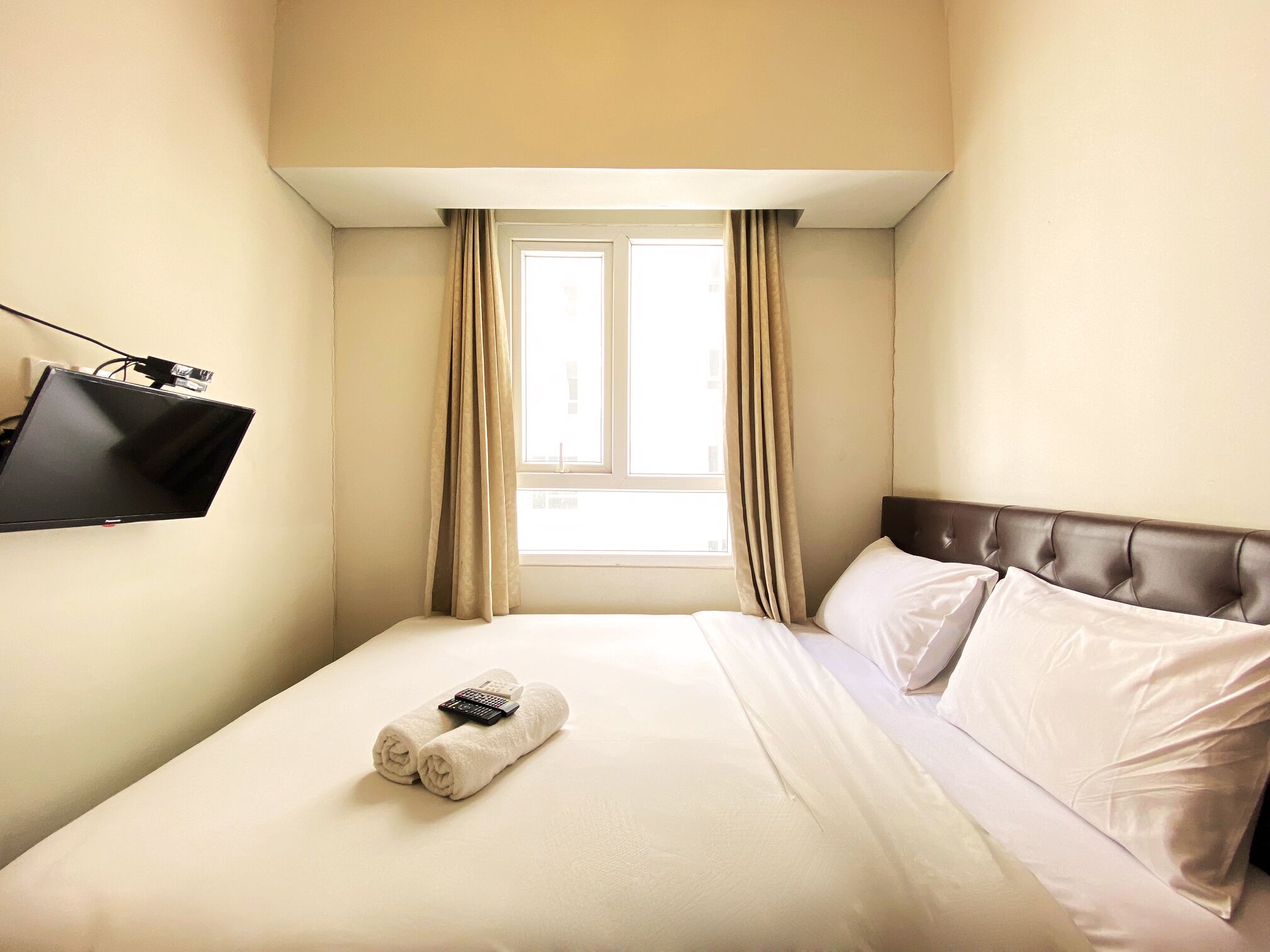 A hotel room with a bed, a TV mounted on the wall, and a window with curtains.
