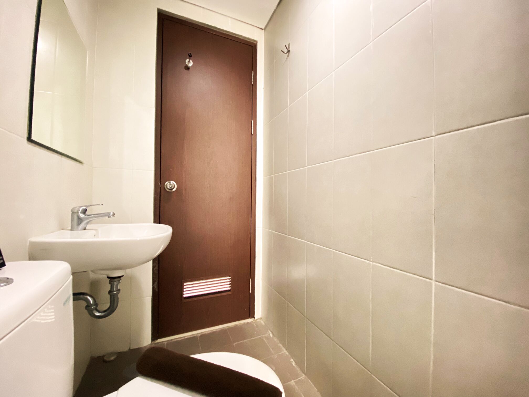 Une petite salle de bain avec un lavabo blanc, des toilettes et une porte marron.
