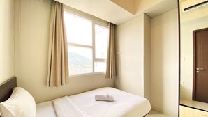 A hotel room with a bed, a wardrobe, a window with curtains, and a view of a mountain. - Fancy And Nice 2Br Apartment At Skyland City Jatinangor (Hegarmanah)