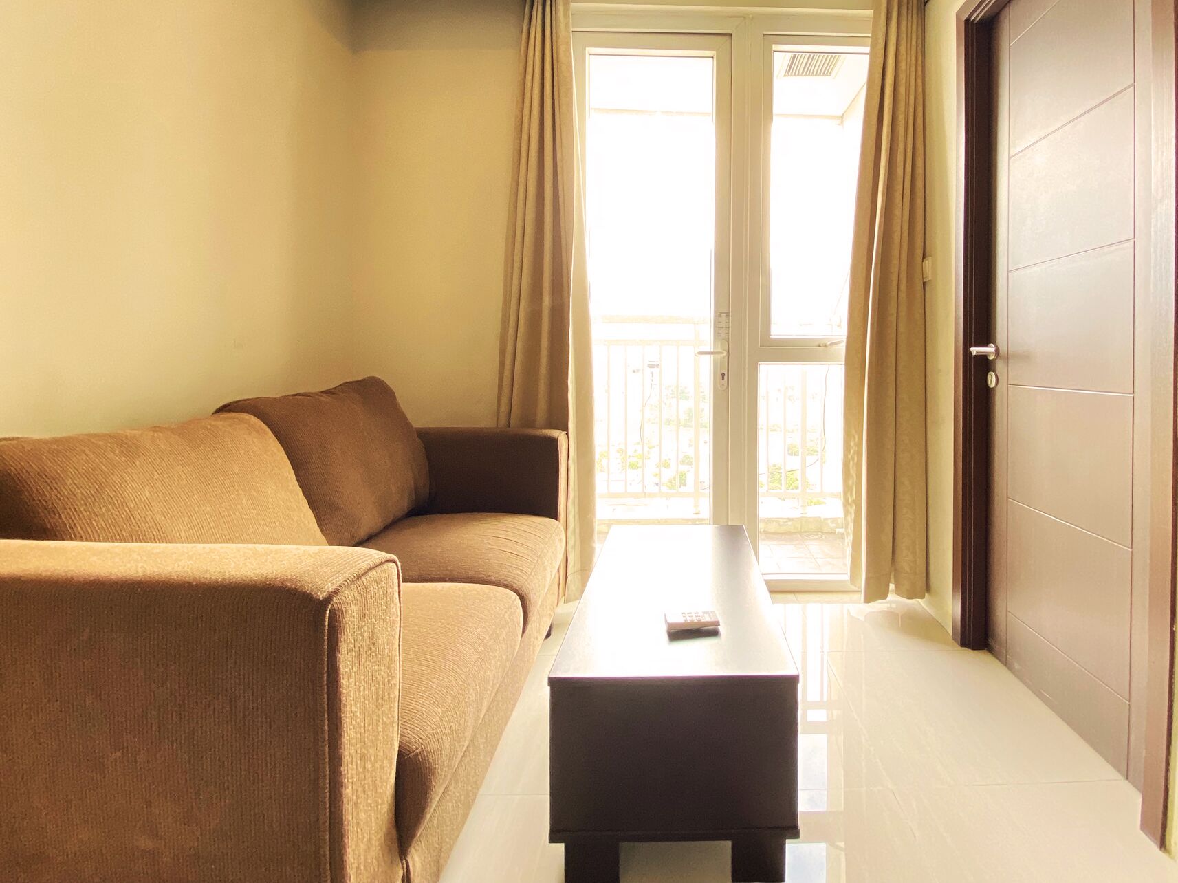 A room with a brown sofa, a small table, and a door leading to a balcony.