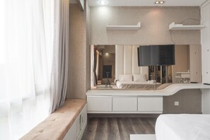 A modern hotel room with a large bed, a built-in bench, a flat-screen TV, and a large window with sheer curtains. - Minimalist And Cozy Studio At Ambassade Kuningan Apartment (Jakarta)