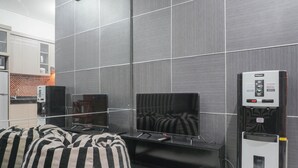 A modern living room with a flat-screen TV, a water dispenser, and striped cushions. - Special 1Br Direct Pool Access At Thamrin Residence (Jakarta)