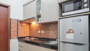 A compact kitchen with a gas stove, a microwave, and a refrigerator. - Special 1Br Direct Pool Access At Thamrin Residence (Jakarta)