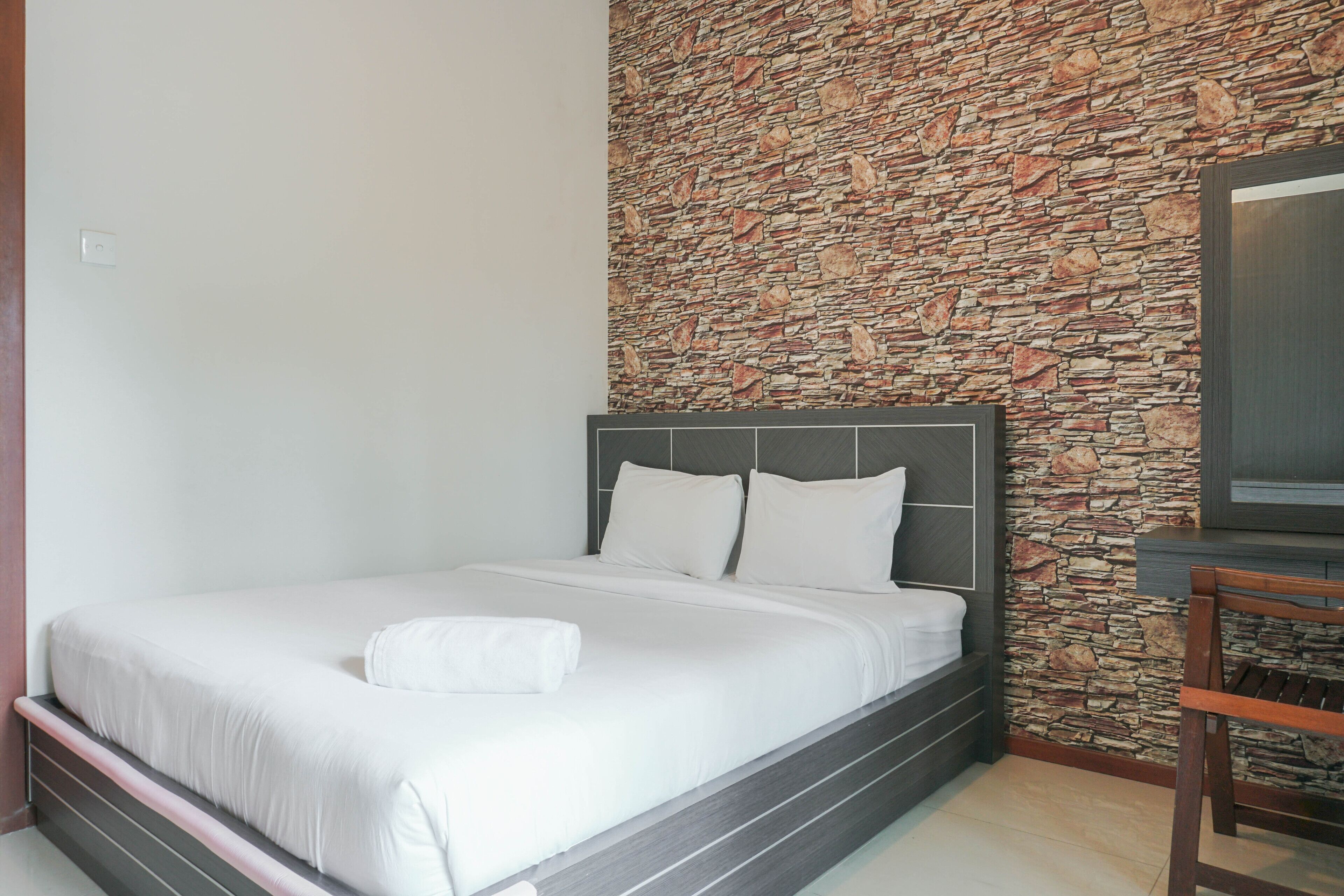 A neatly made bed with white linens in a room with a stone wall and a dark wooden headboard.