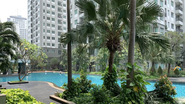 A swimming pool surrounded by lush greenery and tall buildings in the background. - Special 1Br Direct Pool Access At Thamrin Residence (Jakarta)
