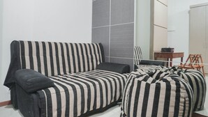 A modern living room with a striped sofa, a small table, and a chair. - Special 1Br Direct Pool Access At Thamrin Residence (Jakarta)