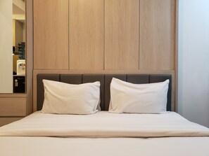 A neatly made bed with two pillows, a wooden headboard, and a small bedside table with a water dispenser. - Tranquil And Nice Studio At Tokyo Riverside Pik 2 Apartment (Teluknaga)