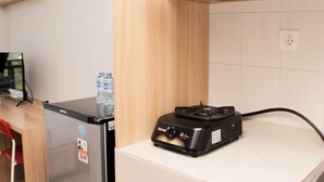 A kitchen with a refrigerator, a water dispenser, and a portable gas stove. - Cozy Studio At Monroe Tower Apartment (Cikarang)