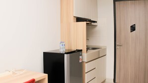A compact kitchen with a refrigerator, a sink, and wooden cabinets. - Cozy Studio At Monroe Tower Apartment (Cikarang)
