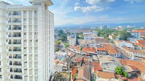 A high-rise building with multiple balconies and a view of a cityscape with various buildings and a mountain in the distance. - Warm And Comfort Studio Apartment At Braga City Walk (Bandung)