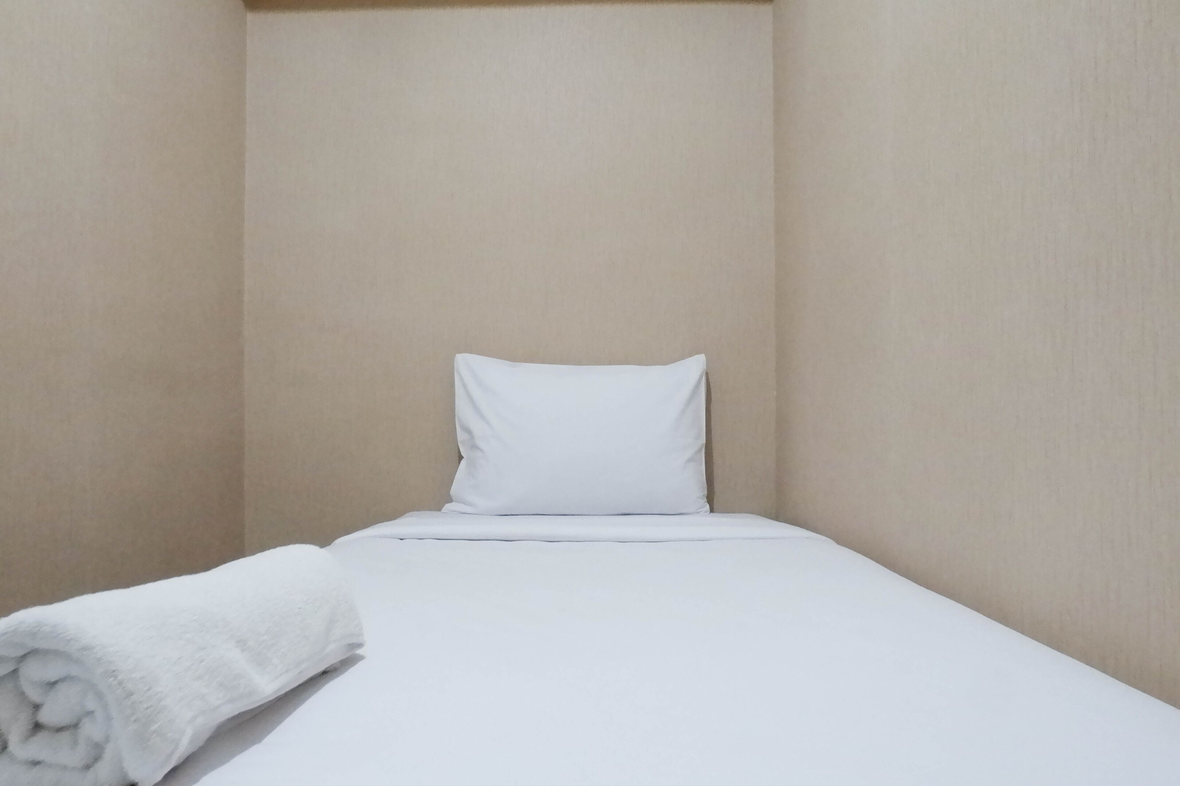 A small, neatly made bed with a white pillow and a rolled white towel.