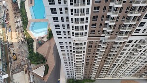 Un edificio alto con varios balcones, una piscina y un área ajardinada con senderos y vegetación.
