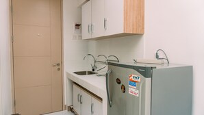 A kitchen with a refrigerator, sink, cabinets, and a door. - Nice And Comfort Studio Apartment At Tokyo Riverside Pik 2 (Jakarta)