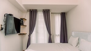 A hotel room with a bed, a flat-screen TV mounted on the wall, and a window with curtains. - Nice And Comfort Studio Apartment At Tokyo Riverside Pik 2 (Jakarta)