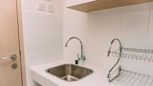 A modern kitchen with a stainless steel sink, a double faucet, and a wire shelf above it. - Nice And Comfort Studio Apartment At Tokyo Riverside Pik 2 (Jakarta)