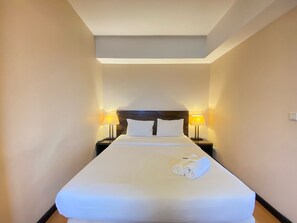 Ein Hotelzimmer mit einem großen Bett, zwei Nachttischlampen und einem ordentlich bezogenen Bett mit einem zusammengerollten Handtuch.