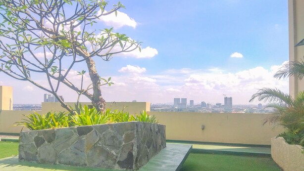 A rooftop garden with a stone planter, green artificial grass, and a view of a city skyline. - Cozy Studio at Lagoon Bekasi Town Square Apartment (Bekasi)