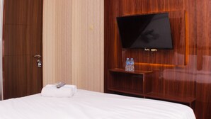 A hotel room with a wooden wardrobe, a flat-screen TV mounted on the wall, a bed with white linens, and a shelf with bottled water. - Cozy Studio at Lagoon Bekasi Town Square Apartment (Bekasi)