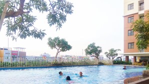 A swimming pool with people in the water, surrounded by buildings and trees. - Cozy Studio at Lagoon Bekasi Town Square Apartment (Bekasi)