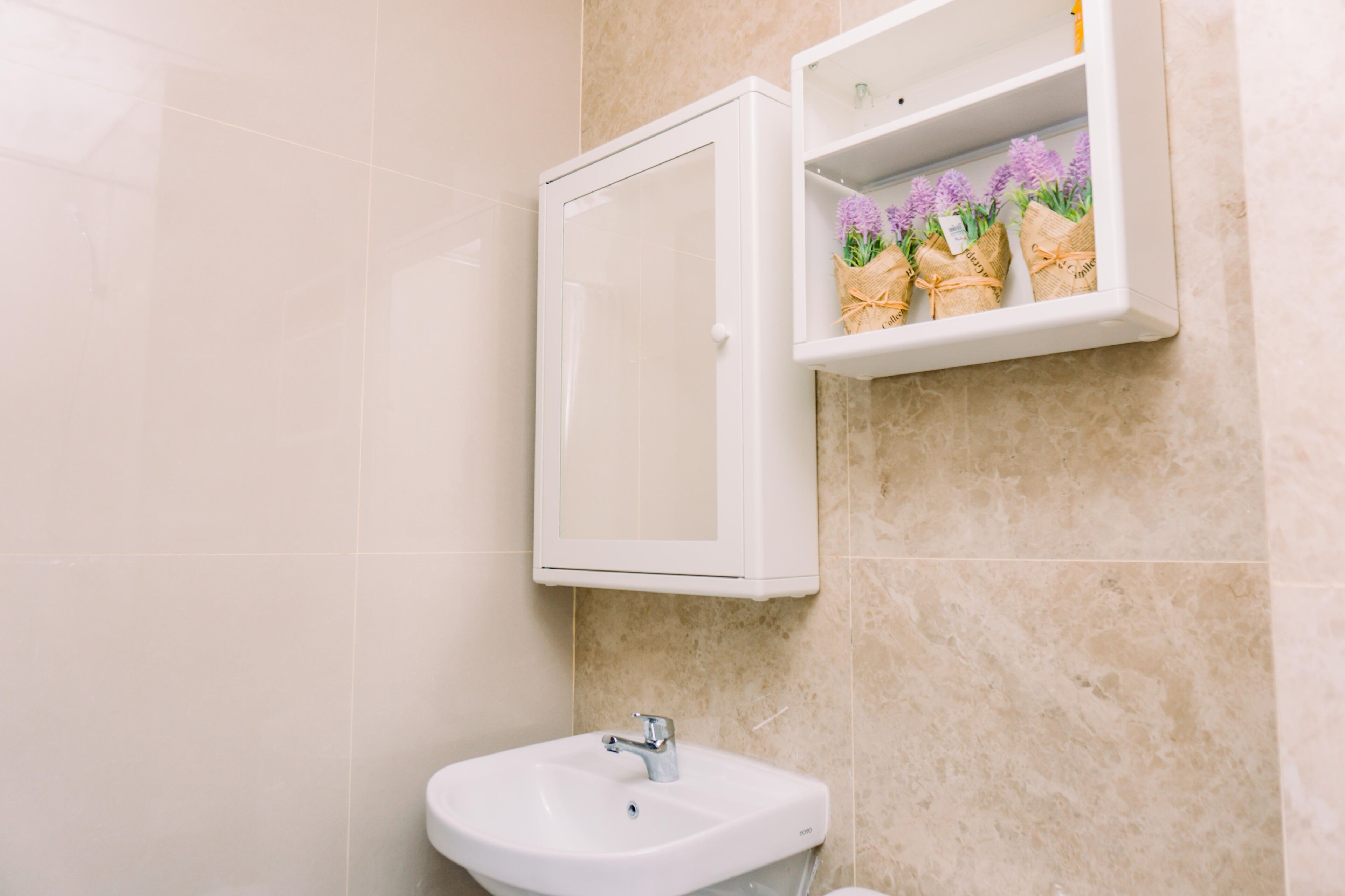 Une salle de bain avec un lavabo blanc, un meuble à miroir et une étagère ornée de fleurs violettes.