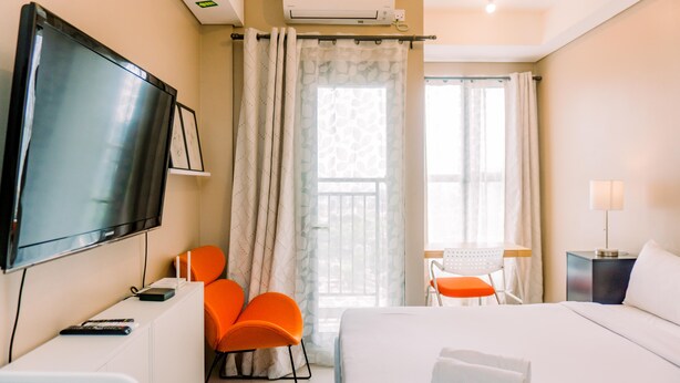 Une chambre d’hôtel avec un lit, une télévision, un bureau avec une chaise et une fenêtre avec des rideaux.