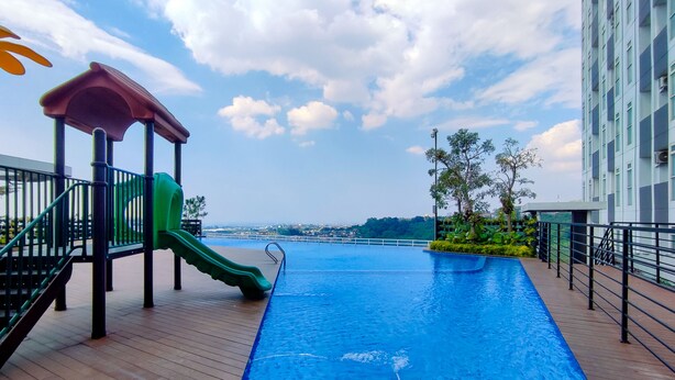 A rooftop pool with a slide, surrounded by a wooden deck and a railing.