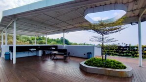An outdoor patio with a wooden deck, a seating area with chairs and a table, and a small tree in a planter.