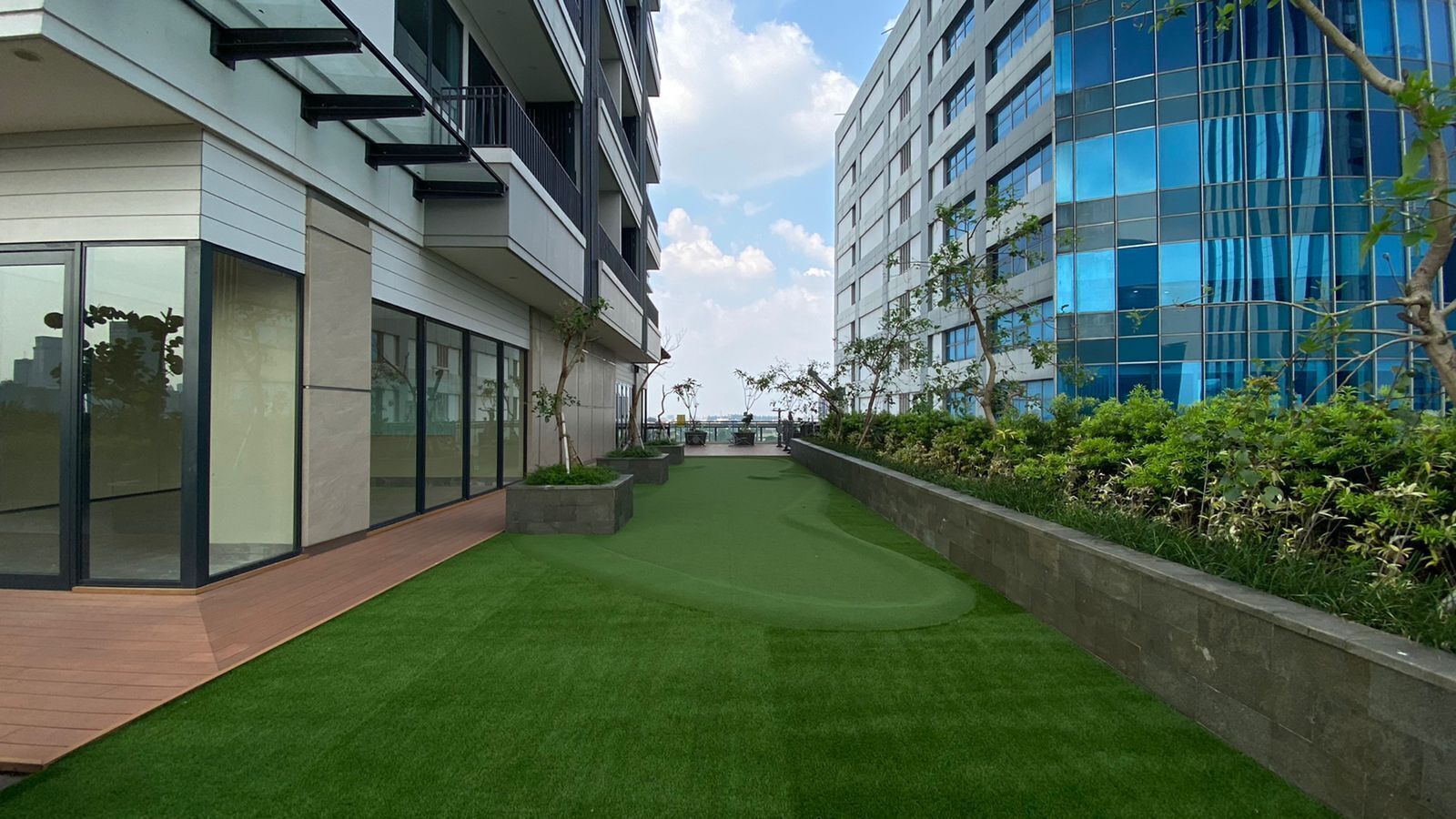A modern building with a rooftop garden, glass windows, and a clear sky.