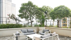 A rooftop patio with white furniture, including a sofa and chairs, surrounded by greenery and a view of buildings. - Comfy 1Br At Bellezza Apartment (Jakarta)
