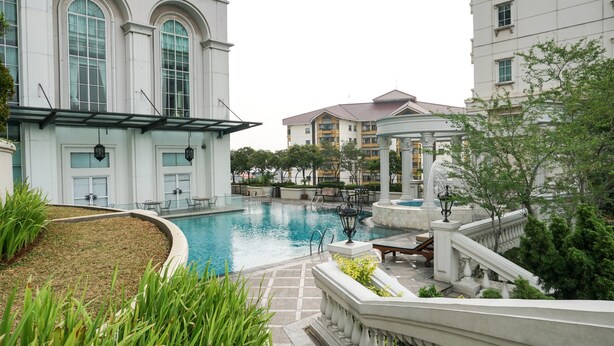 A swimming pool surrounded by buildings with large windows and a fountain. - Comfy 1Br At Bellezza Apartment (Jakarta)