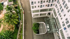 An aerial view of a modern building with a parking area, surrounded by greenery and palm trees. - Minimalist 2Br Apartment At Serpong Garden Near Train Station (Cisauk)