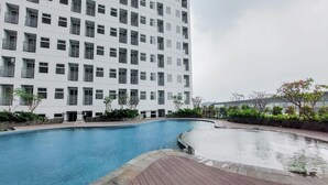 A modern building with a swimming pool and a wooden deck area. - Minimalist 2Br Apartment At Serpong Garden Near Train Station (Cisauk)