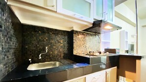 A modern kitchen with a black countertop, white cabinets, and a tiled backsplash. - Relaxing Studio Room At Suites @Metro Apartment (Bandung)
